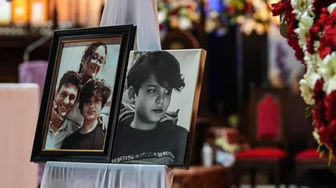 Minguzzi'nin iki fotoğrafı bir standın üzerinde etrafında seremoni çiçekleri ve arka olanda sandalyeler görünüyor.