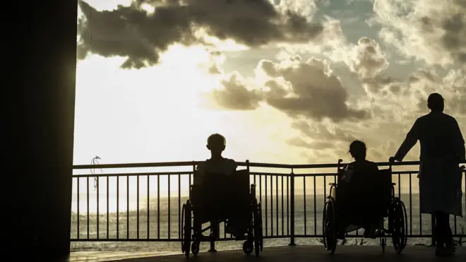 Pacientes e acompanhantes observam o pôr-do-sol em píer do hospital Mont Serrat