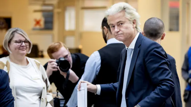 Герт Вилдерс смотрит в камеру, опуская бюллетень в урну.