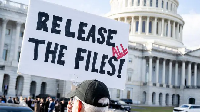 Man holding a sign that says "release all the files" with a black hat on standing outside the US Capitol on 12 November.