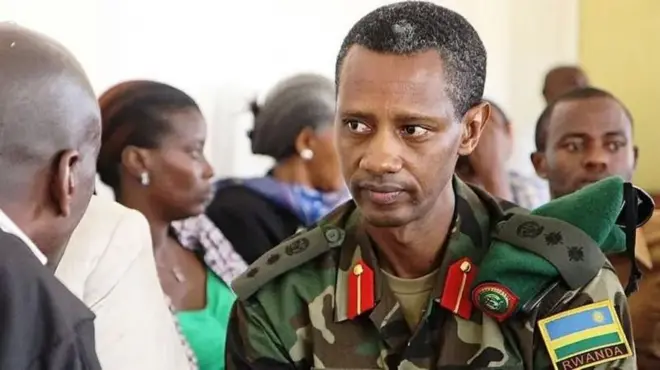 Tom Byabagamba yambaye imyenda ya gisirikare akikijwe n'abandi bantu ari mu rukiko. Arareba muri 'camera'. Ifoto mbarankuru yo mu bubiko, yafotorewe mu rukiko rwa gisirikare i Kigali, mu Rwanda, ku itariki ya 29 Kanama (8) mu mwaka wa 2014. 