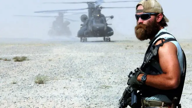 ทหารสหรัฐฯ ถือปืน ฉากหลังเป็นเฮลิคอปเตอร์