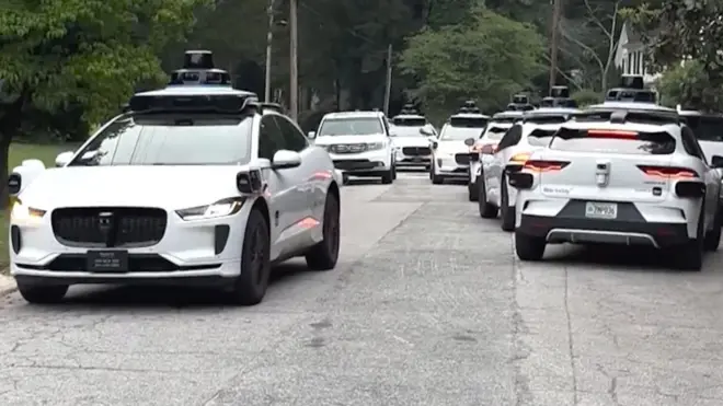 A litany of Waymo cars take up all the space in a street.