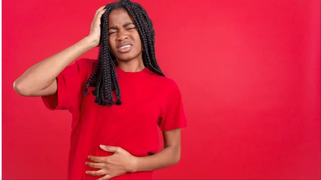 Aworan obinrin kan to wọ aṣọ pupa to si di ori mu pẹlu ọwọ ọtun, di inu mu pẹlu ọwọ osi