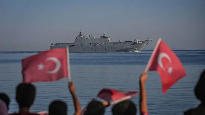 Çocukların flu bayran sallayan görüntüleri önde, hepsinin arkası dönük denizden geçen gemiye bakıyorlar.