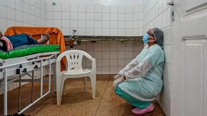 Profissional de saúde sentado de cócoras na frente de um paciente que sofre com complicações da covid-19