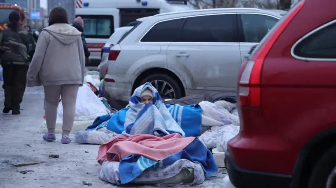 Жінка закутана в ковдри сидить біля машин на вулиці