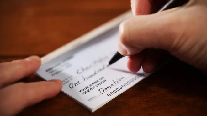 Persona escribiendo un cheque de US$100