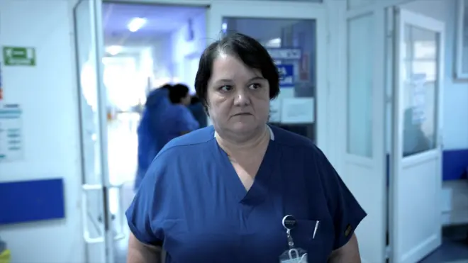 Cerrah Dr. Oana Goidescu Buzău Hastanesi'nde mavi önlüğüyle vardiyada. Orta uzunlukta siyah saçları var