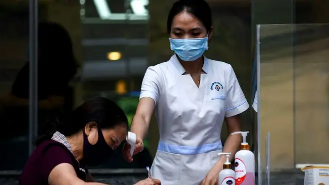 Nhân viên y tế kiểm tra thân nhiệt một người đang khai báo y tế tại một bệnh viện đa khoa ở Hà Nội hôm 05/5/2021