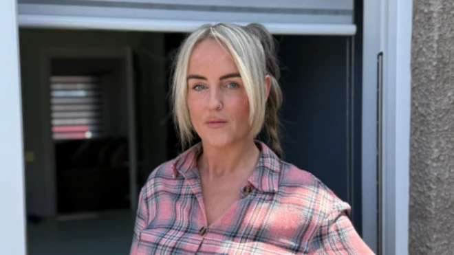 A woman with blonde hair tied up in a ponytail is wearing a pink and grey checked shirt