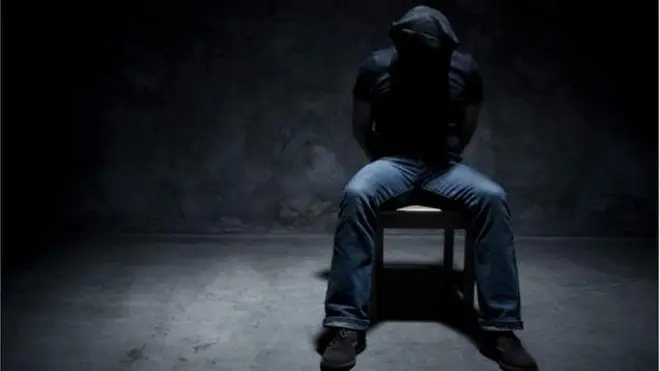 Man wey dem tie im hand behind im back siddon ontop chair