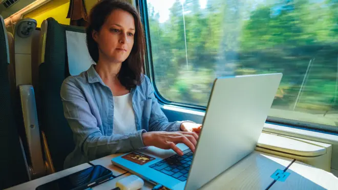 Biznesmenka siedzi przy stoliku w pociągu, pracując na laptopie podczas podróży