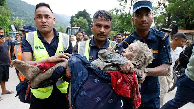 Rescatistas cargan a una anciana cubierta de barro en Nepal.