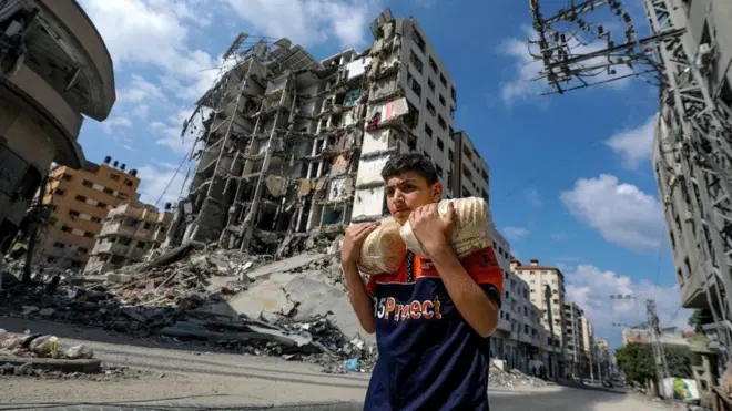 Um jovem palestino carregando pão na Cidadesportingbet welcome offerGaza, caminhando entre prédios destruídos