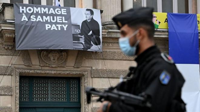 A French police officer stands next to a portrait of French teacher Samuel Paty