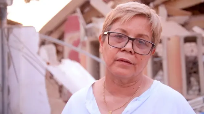 Zuly Marín, dressed in a white shirt and black glasses, stares into space.