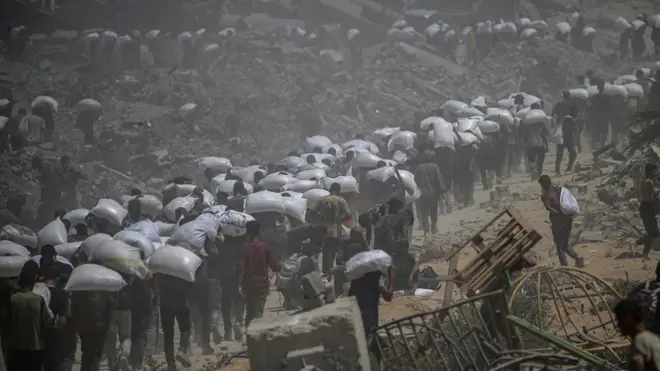 فلسطينيون يحملون أكياساً من الدقيق بالقرب من نقطة توزيع المواد الغذائية في معبر زيكيم في 27 يوليو/تموز 2025