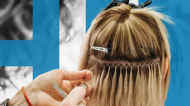 A hair stylist attaches hair extension links to a woman's natural hair in a salon