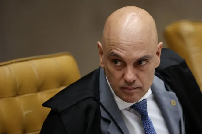 Moraes sentado um pouco inclinado para frente com semblante sério e a sombrancelha direita levantada, durante sessão no plenário do STF. Ele veste terno cinza, gravata azul e toga de juiz. 