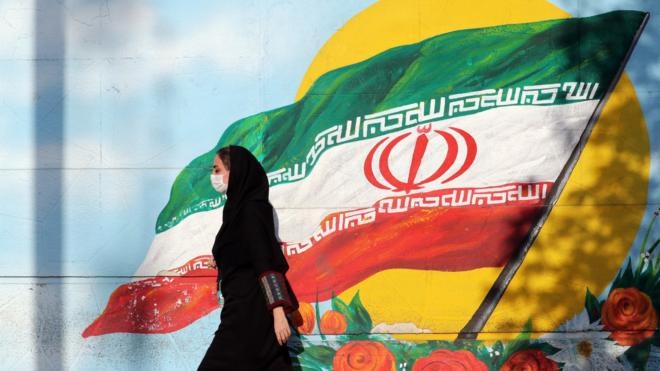 伊朗德黑蘭街頭一名戴著口罩的女子走過一幅伊朗國旗壁畫（28/7/2020）