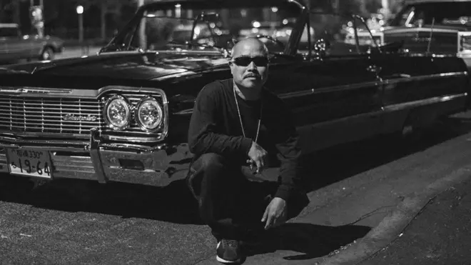 Chicano japonés frente a su auto "lowrider"