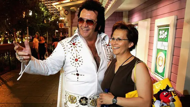 El imitador de Elvis Presley Tom E. Lynd (izquierda) posa para una foto con la turista canadiense Brenda Rediron en el Strip el 28 de junio de 2005 en Las Vegas, Nevada. Lynd es dueño de Legends in Photos, un grupo de imitadores que se presentan en el Strip y posan con los turistas a cambio de propinas. (Foto de Ethan Miller/Getty Images)