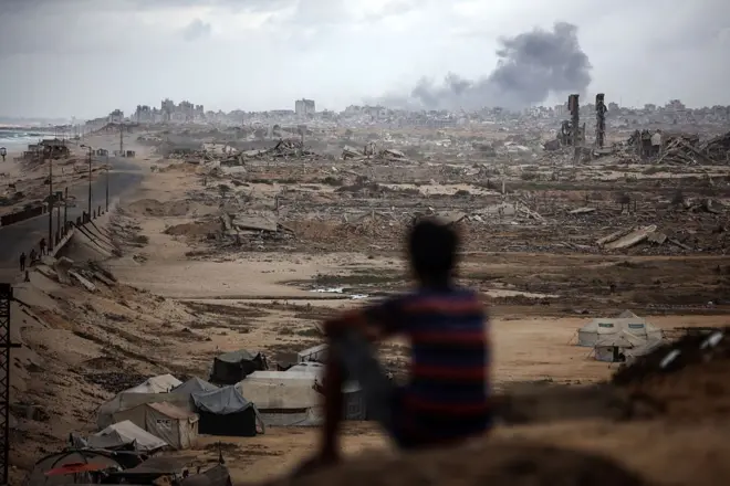 Image floutée d'un enfant assis sur des décombres comptemplant une fumée au loin
