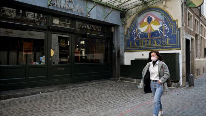 A woman in a mask walks past a closed restaurant in Brussels