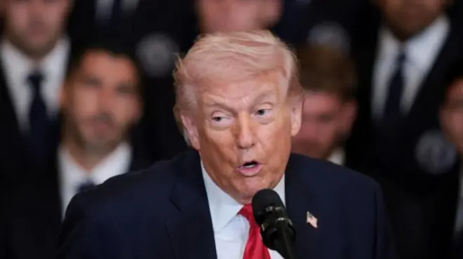 ダークスーツに赤いネクタイを着けたトランプ米大統領が、マイクに向かって話している