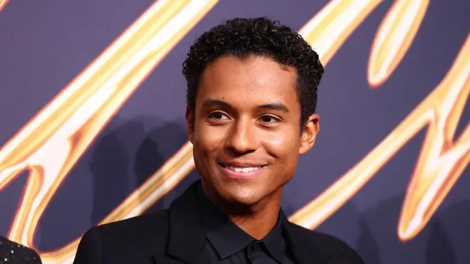 Jaafar Jackson sonríe mirando hacia un costado con un fondo alusivo a la película "Michael" detrás.