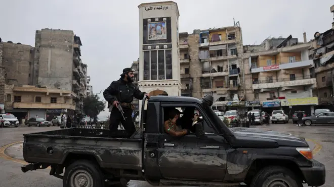 Bir pikap araç üzerinde ayakta duran silahlı bir Suriye ordu mensubu ve arkada Eşrefiye mahallesi