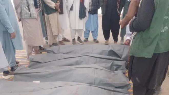 چند نفر در کنار جسدهایی که به تازگی از ایران به افغانستان منتقل شده ایستادهاند. اجساد درون کیسه قرار دارند.