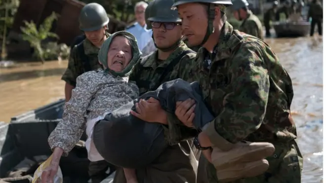 Seorang perempuan dievakuasi dari lokasi banjir oleh para personel militer Jepang di Kurashiki, Prefektur Okayama, Minggu (8/7).