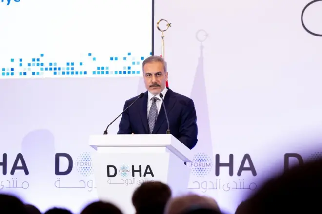 Hakan Fidan mor-beyaz bir arka planın önünde, kürsüde konuşuyor.