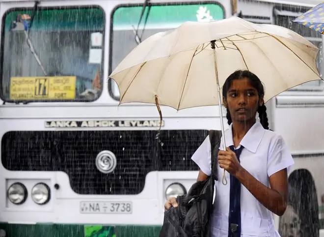 A Sri Lankan schoolgirl holds an umbrella as she walks through a downpour in Colombo 