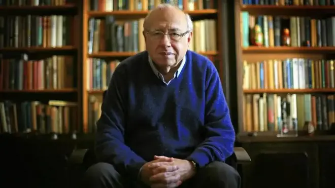 Luis Fernando Verissimo sentado em frente a uma estante de livros.