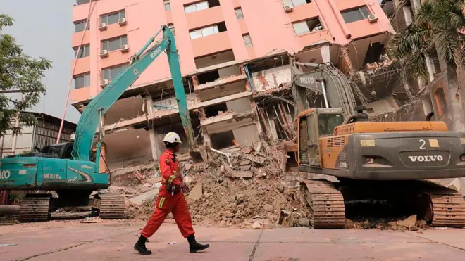 Một nhân viên cứu hộ đi ngang qua các thiết bị xây dựng hạng nặng đang được sử dụng để dọn dẹp đống đổ nát tại hiện trường một tòa nhà bị sập ở Mandalay ngày 5 tháng 4 năm 2025, sau trận động đất xảy ra hôm 28 tháng 3.