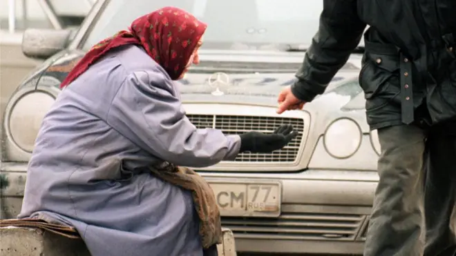 Пожилая женщина просит милостыню, сидя возле автомобиля Mercedes-Benz. Москва, 25 декабря.