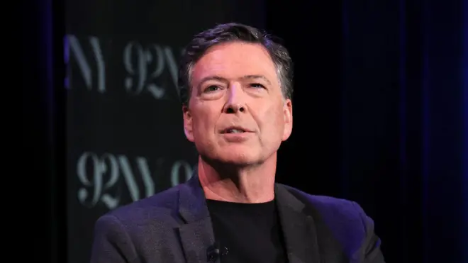 Джеймс Коми в черном пиджаке и черной водолазке с небольшим микрофоном на лацкане.