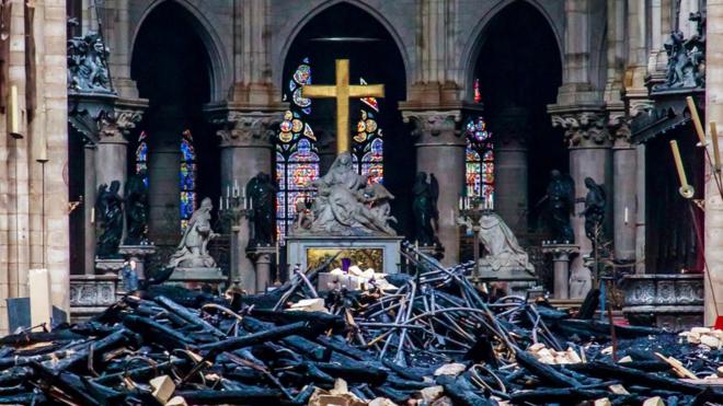 A view of the cross and sculpture of Pieta by Nicolas Coustou in the background of debris inside Notre-Dame de Paris