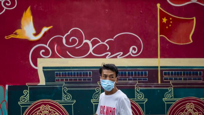 上海街头一位戴着口罩的男子走过一面中国形象宣传壁画（6/8/2020）