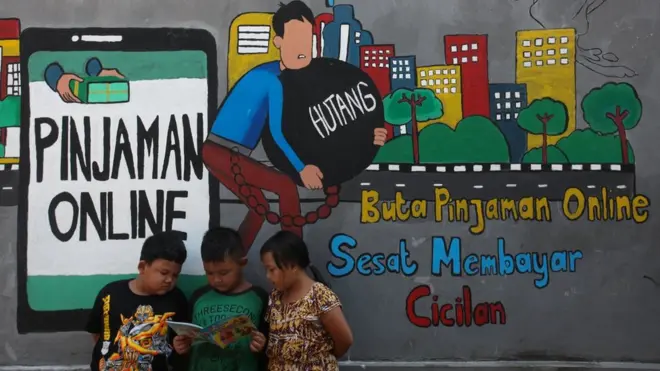 Sejumlah anak membaca bersama di dekat dinding bermural di kawasan Tempurejo, Surabaya, Jawa Timur, Selasa (7/9/2021). Mural tersebut sebagai sarana imbauan kepada masyarakat terhadap bahaya pinjaman daring atau 'online' (pinjol) ilegal yang sekarang lagi marak