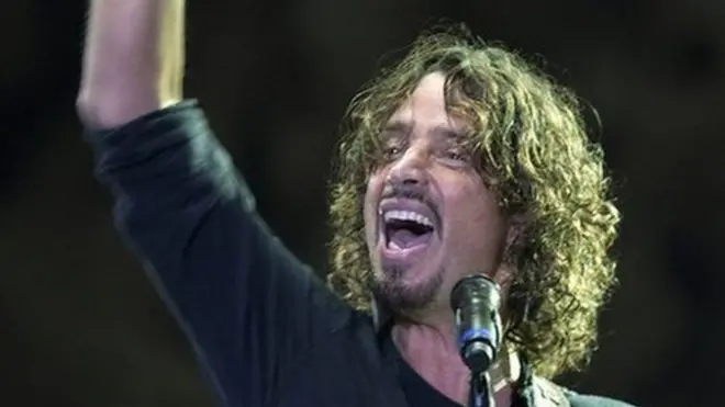 Chris Cornell on stage, raising his hand high as he plays guitar
