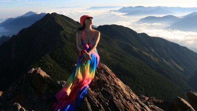 A alpinista Gigi Wu sentada no topo de uma montanha. Ela morreu de hipotermia depois de se ferir durante uma escalada