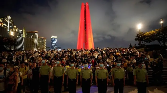 Paramilitary police and police officers keep watch as people gather to they watch a light show celebrating the 100th founding anniversary of the Communist Party of China at The Bund in Shanghai, China, on 30 June 2021