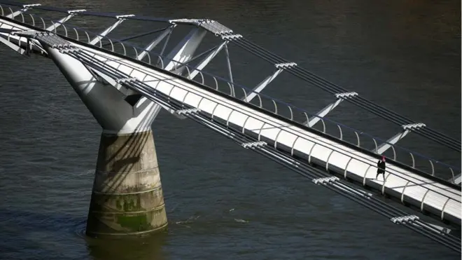 Seorang perempuan berjalan melintasi Jembatan Milenium yang kosong selama jam sibuk London. Perdana Menteri Boris Johnson mengatakan semua orang di Inggris harus menghindari perjalanan "tidak penting" dan kontak dengan orang lain untuk mengendalikan penyebaran virus corona.