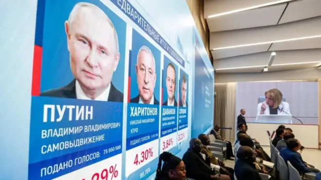Интернатионал обсерверс сит ин фронт оф а сцреен схоwинг прелиминарy ресултс оф тхе пресидентиал елецтионс ат тхе Централ Елецтион Цоммиссион ин Мосцоw, Руссиа