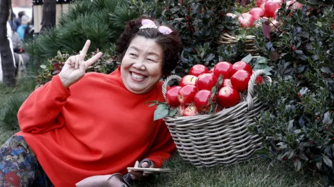 Une femme posant tout sourire devant un panier de pommes rouges