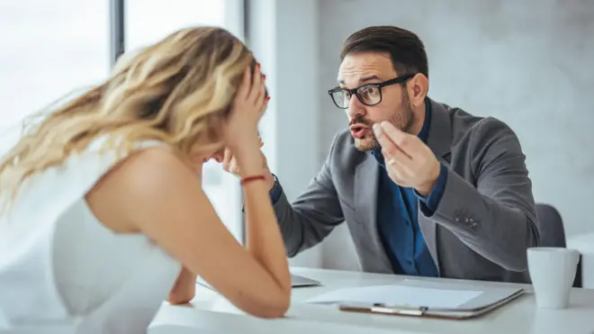 Mężczyzna krzyczy na kobietę w biurze, oboje siedzą przy biurku